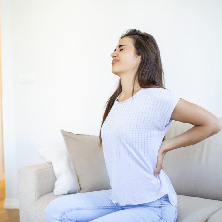 Woman suffering from backache at home. Lower Back Pain . Woman feels back pain massaging aching muscles, sad woman suffers from low-back